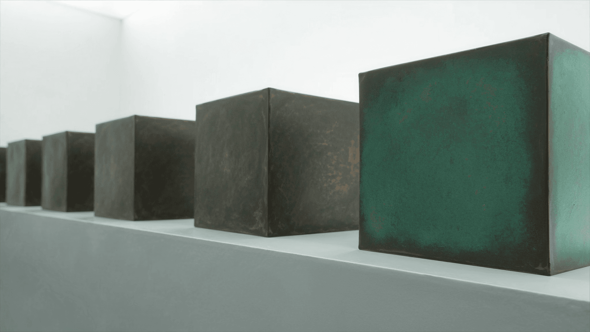 Four ascending modular units on a chalk-white display surface under skylight, the tallest finished in emerald-patinated copper