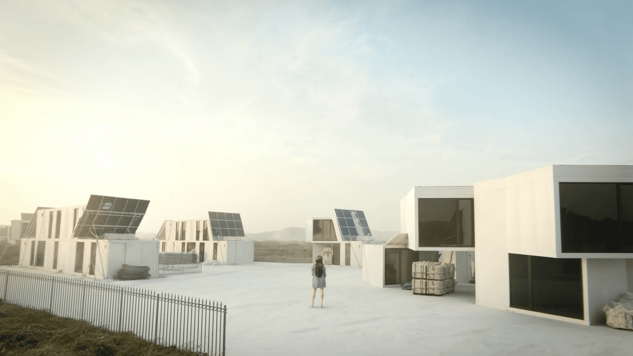 Sunrise over a row of solar-panel-clad modular units in an Irish landscape, pale morning sky, soft golden-hour light